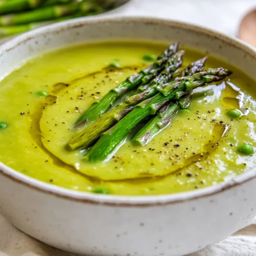 Bowl Of Creamy Asparagus Soup Garnished With Roasted Asparagus Tips And Black Pepper On A White Towel