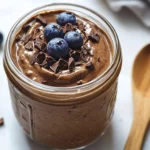 Mason Jar Of Creamy Chocolate Protein Overnight Oats Topped With Cacao Nibs And Blueberries