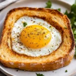 Golden Egg In A Hole Served On A White Plate With Cracked Pepper And Parsley Garnishes