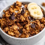 Bowl Of Grain-Free Banana Bread Granola With Dark Chocolate Chips And Banana Slices, Garnished With Flaxseeds