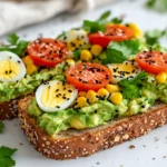Guacamole Breakfast Toast On A White Plate Topped With Charred Corn, Hard-Boiled Eggs, And Parsley