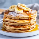 Fluffy Healthy Banana Pancakes Drizzled With Maple Syrup And Topped With Blueberries On A White Plate