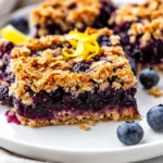 Healthy Blueberry Crumble Bars On A White Plate, Garnished With Fresh Blueberries And Lemon Zest