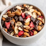 Bowl Of Healthy Dark Chocolate Trail Mix With Cashews, Almonds, Strawberries, And Dark Chocolate Chunks On A White Plate
