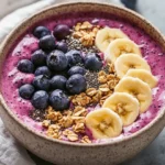 Bowl Of Healthy Smoothie Bowl Topped With Banana, Berries, Granola, And Chia Seeds, Served On A Neutral Background.