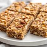Homemade Protein Bars Served On A White Plate, Showcasing A Nutty Texture And Garnished With A Drizzle Of Maple Syrup.