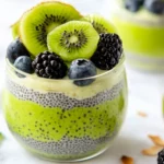 Layered Kiwi Chia Pudding In A Glass Topped With Kiwi Slices, Blueberries, And Toasted Coconut Flakes.
