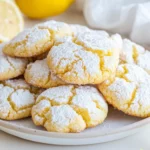 Plate Of Soft Lemon Crinkle Cookies Dusted With Powdered Sugar, Garnished With Lemon Wedges