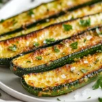 Crispy Oven Roasted Zucchini Sticks On A White Plate, Garnished With Fresh Parsley And Sea Salt