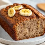 Slice Of Paleo Almond Flour Banana Bread On A White Plate, Garnished With Banana Slices And Cinnamon