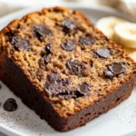 Slice Of Paleo Chocolate Chip Banana Bread On A White Plate Garnished With Fresh Banana Slices And Cocoa Powder