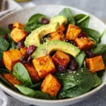 Delicious Sweet Potato Salad With Spinach, Avocado, And Cranberries In A White Bowl, Garnished With Hemp Seeds.
