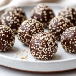 Plate Of Tahini Chocolate Balls Coated In Sesame Seeds, Set Against A Neutral Background