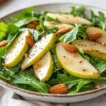 Asiago Arugula Salad With Pears, Avocado, And Toasted Almonds On A White Plate Garnished With Basil