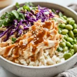 Close-Up Of Asian Chicken Rice Bowl With Shredded Chicken, Edamame, And Coleslaw In A White Bowl