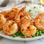 Baked Coconut Shrimp On A White Plate With Jasmine Rice, Drizzled With Honey Butter Sauce And Peas