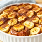 Delicious Banana Bread Pudding In A White Dish, Topped With Caramel Sauce And Sliced Bananas