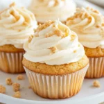 Banana Pudding Cupcakes Topped With Whipped Cream And Crushed Vanilla Wafers On A White Plate.