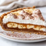 Delicious Banoffee Pie On A White Plate With Whipped Cream, Banana Slices, And Chocolate Shavings