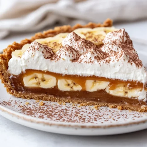 Delicious Banoffee Pie On A White Plate With Whipped Cream, Banana Slices, And Chocolate Shavings