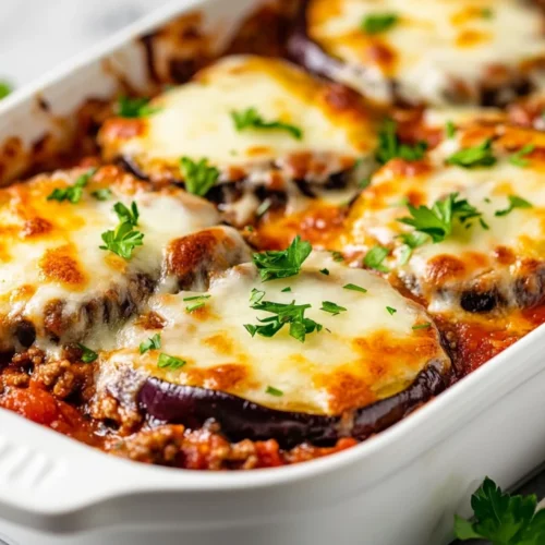 Layered Beef Eggplant Parmesan In A White Baking Dish, Topped With Melted Cheese And Parsley Garnish