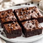 Decadent Black Bean Brownies On A White Plate, Topped With Melted Chocolate And A Sprinkle Of Chocolate Chips.