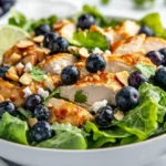 Blueberry Goat Cheese Chicken Salad In A White Bowl Topped With Blueberries, Goat Cheese, And Peanut Dressing