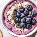 Bowl Of Blueberry Overnight Oats Topped With Fresh Blueberries And Chia Seeds Against A Neutral Background