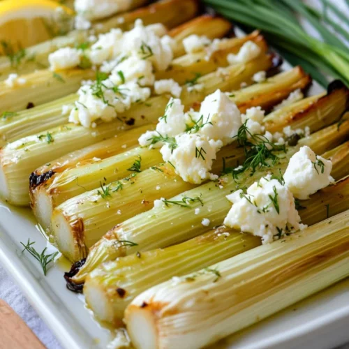 Braised Leeks With Lemon And Feta On A White Plate, Garnished With Chives And Lemon Slices