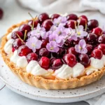 Cherry Angel Pie With Whipped Cream And Cherries On A White Plate, Garnished With Edible Flowers.