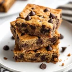 Delicious Chocolate Chip Banana Bread Bars Stacked On A White Plate Garnished With Crumbs And A Kitchen Towel