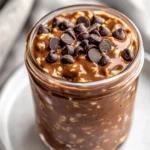 Glass Jar Of Chocolate Peanut Butter Overnight Oats Topped With Mini Chocolate Chips On A White Plate