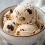 Bowl Of Chunky Banana Ice Cream With Walnuts And Raisins, Garnished With Shredded Coconut On A Simple Surface