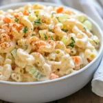Bowl Of Classic Macaroni Salad With Vegetables And Hard-Boiled Egg Garnished With Paprika On A Wooden Table