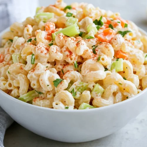 Bowl Of Classic Macaroni Salad Garnished With Hard-Boiled Egg And Paprika On A White Plate