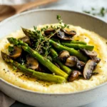 Creamy Polenta With Spring Vegetables In A White Bowl, Topped With Asparagus And Mushrooms, Garnished With Fresh Thyme