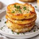 Crispy Cacio E Pepe Potato Stacks Garnished With Parsley And Black Pepper On A White Plate
