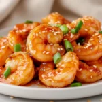 Firecracker Shrimp On A White Plate Garnished With Green Onions And Sesame Seeds, Glistening With Sauce