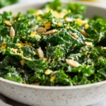 Close-Up Of Garlicky Kale Salad In A White Bowl, Topped With Lemon Zest And Sunflower Seeds