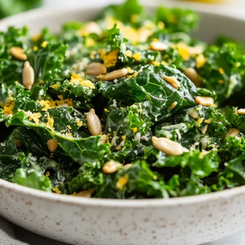 Close-Up Of Garlicky Kale Salad In A White Bowl, Topped With Lemon Zest And Sunflower Seeds