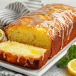 Sliced Glazed Lemon Bread On A White Plate, Decorated With Fresh Lemon Slices And Mint Leaves