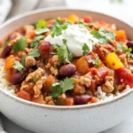 Bowl Of Healthy Chicken Chili Topped With Greek Yogurt And Cilantro Over Brown Rice On A White Table.