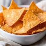 Bowl Of Homemade Tortilla Chips Seasoned With Chipotle, Served With A Beige Kitchen Towel On A Neutral Background