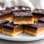 Homemade Twix Bars On A White Platter, Showing Layers Of Caramel And Chocolate, Garnished With Flaky Sea Salt