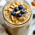 Honey Almond Overnight Oats In A Glass Jar Topped With Sliced Almonds And Blueberries On A Kitchen Towel