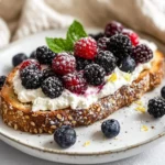Mascarpone Berry Toast On A White Plate Topped With Fresh Berries, Lemon Zest, And Powdered Sugar.