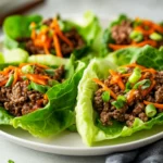 Colorful Orange Beef Lettuce Wraps On A White Plate Filled With Seasoned Beef, Shredded Carrots, And Green Onions.