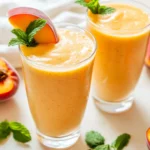 Chilled Peach Smoothie In Clear Glasses Garnished With Peach Slices And Mint Leaves.