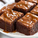 Thick, Fudgy Salted Caramel Brownies On A White Plate Drizzled With Caramel And Sprinkled With Sea Salt.