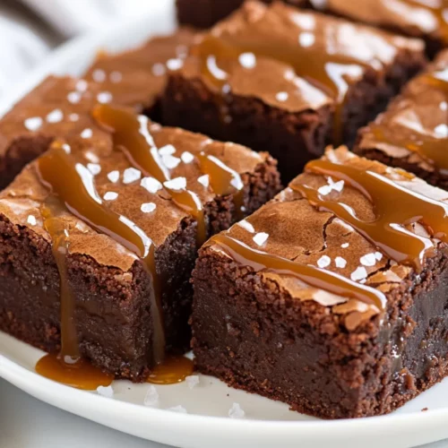 Thick, Fudgy Salted Caramel Brownies On A White Plate Drizzled With Caramel And Sprinkled With Sea Salt.